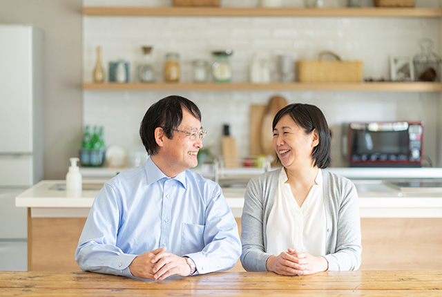 キッチン前に隣同士に座って談笑する50代夫婦