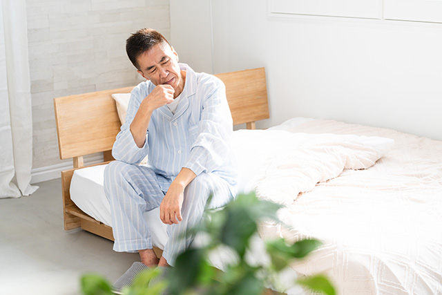 睡眠不足や疲労に悩みベッドに座り頭を抱える中年男性