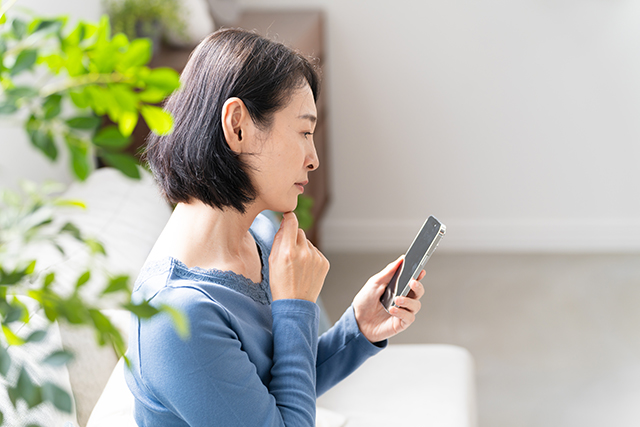 スマートフォンを見ながら悩む女性